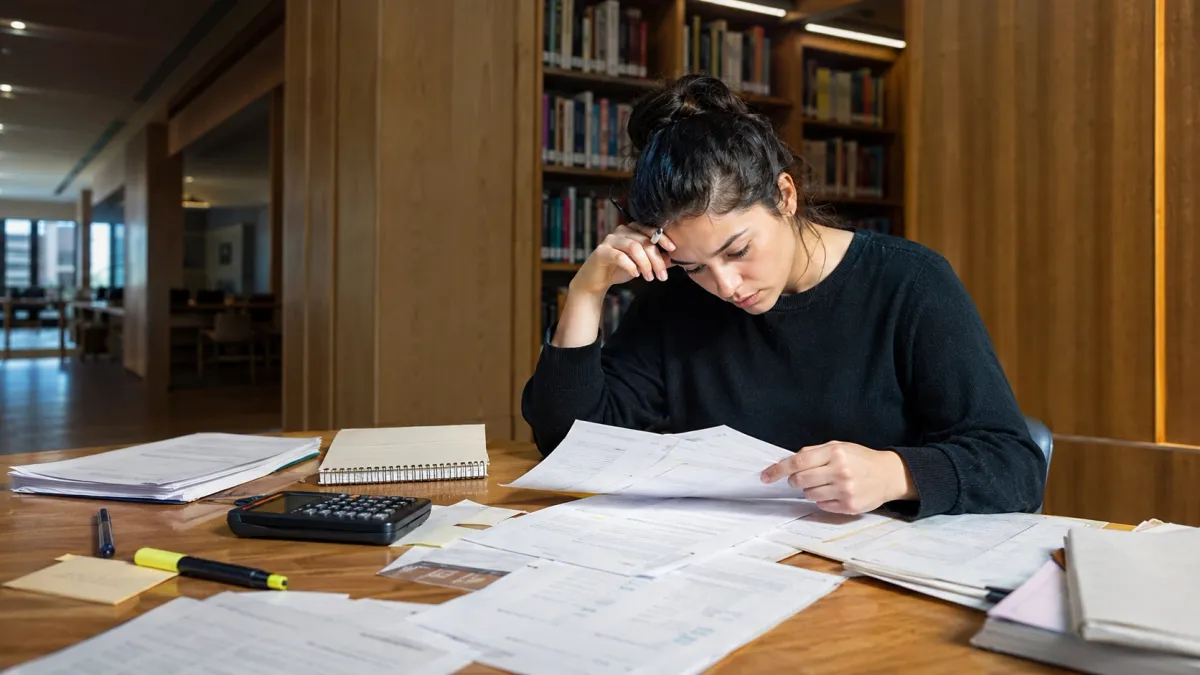 Real estate exam learner sorting a checklist and study pages at a desk during a focused review session.