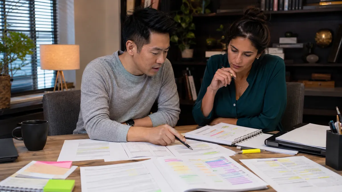 Two adult learners comparing scenario-based real estate exam notes across a table.